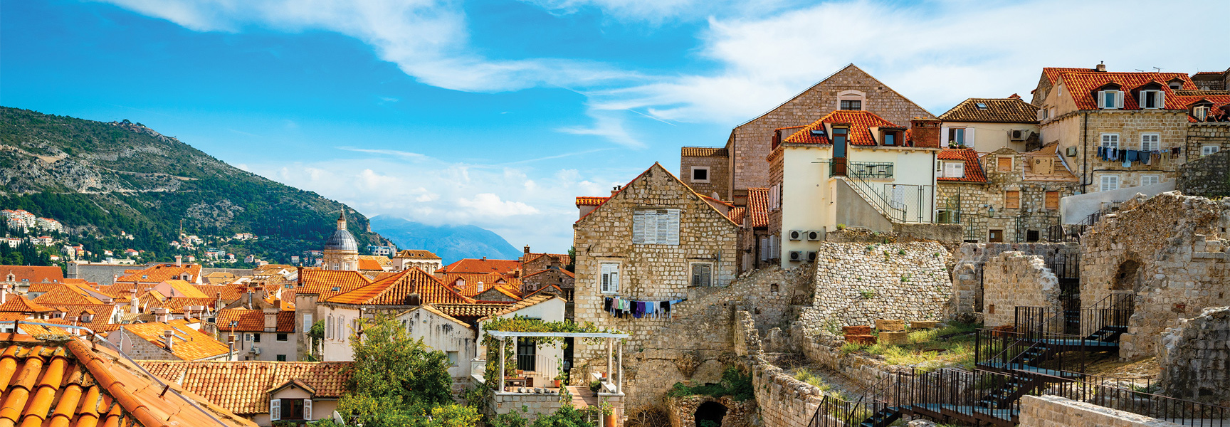 A scenic view of the old stone buildings with red-tiled roofs along the coast of Croatia, with green mountains in the background.