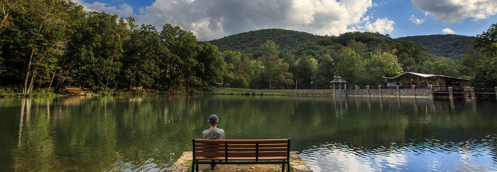 A person sits on a bench overlooking a serene lake and forested mountains at the Montreat Conference Center in North Carolina.