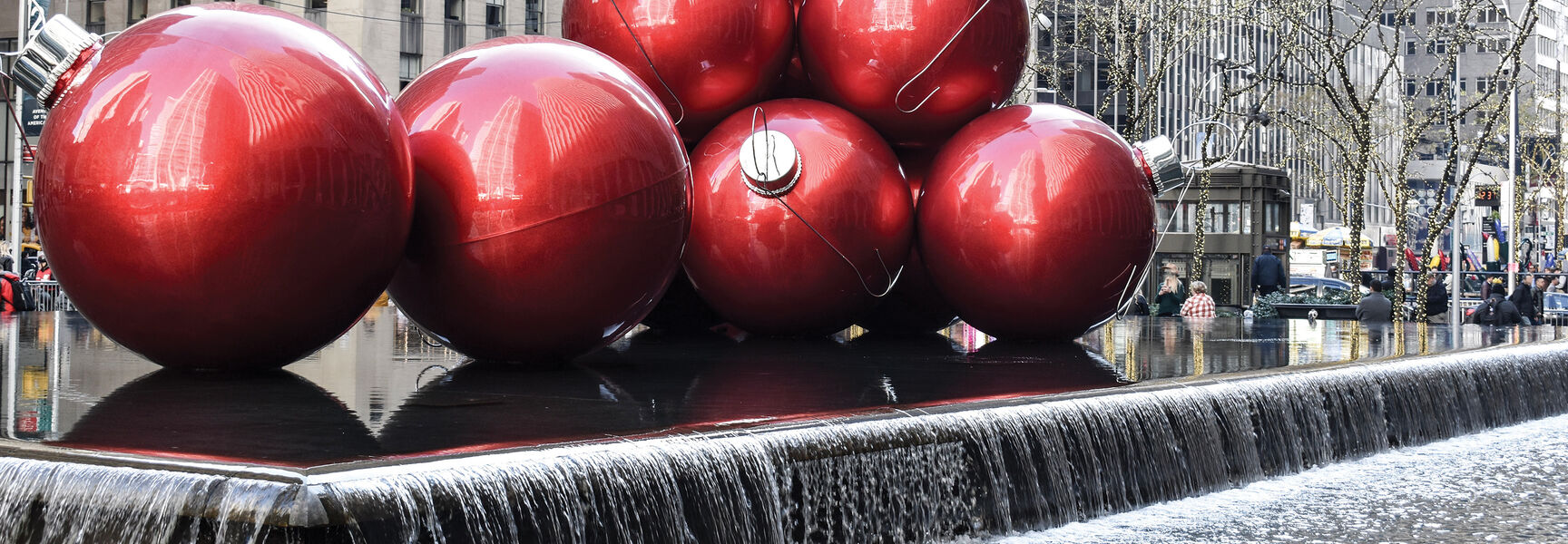 Giant shiny red Christmas ornaments stacked in a fountain pool at Rockefeller Plaza as festive holiday decorations in New York City.