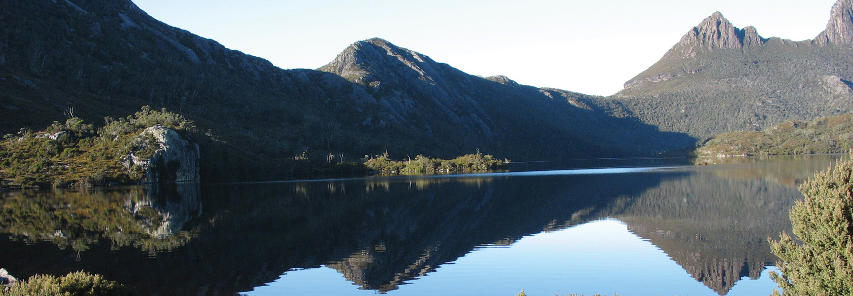 A rugged mountain range in Tasmania, Australia, with its peaks reflected in the still water of a pristine lake below.