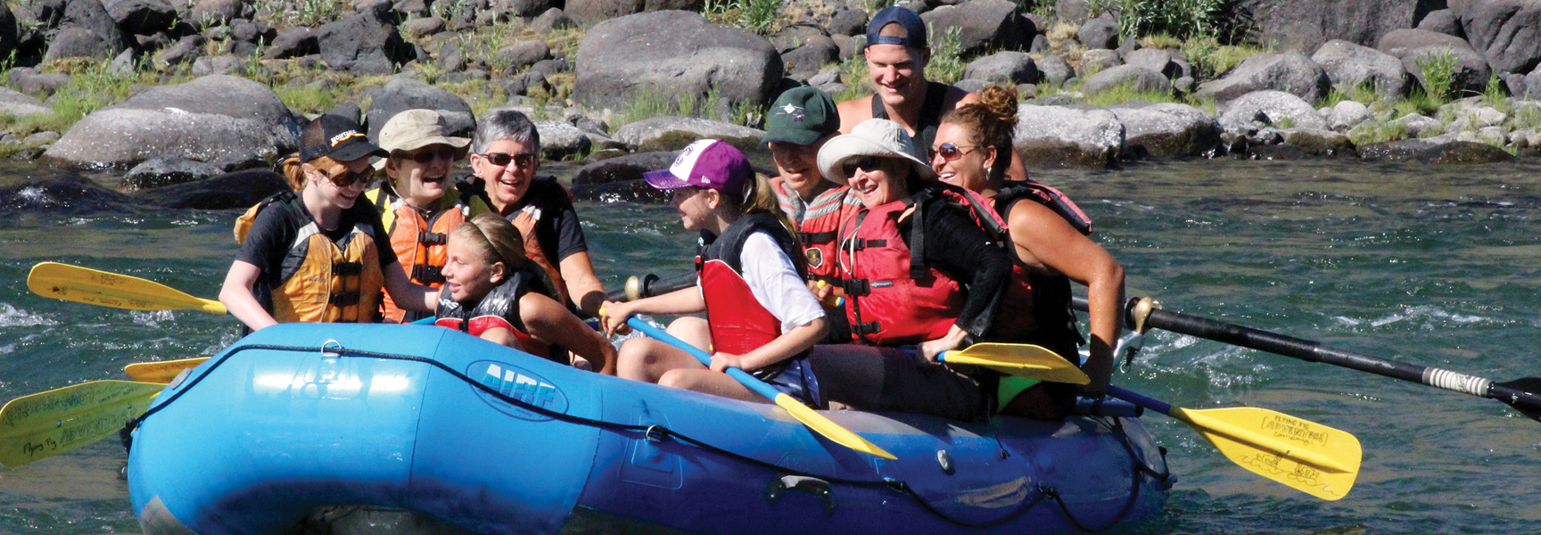 A family joyfully rafts down the Yellowstone River in Montana, surrounded by a rocky shoreline.