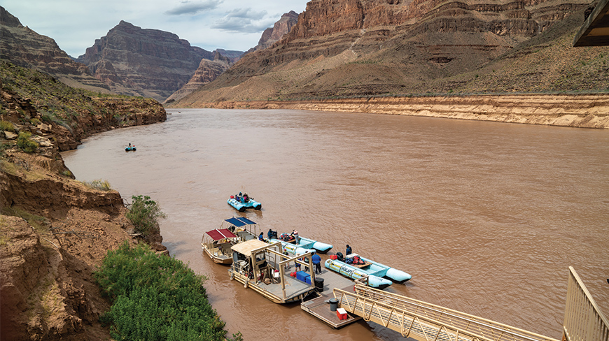 Tourists on several rafts and motorized boats are docked on the Colorado River, preparing for a trip through the Grand Canyon in Arizona.