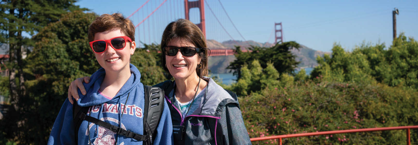 A grandmother and her grandchild smile together in San Francisco, with the Golden Gate Bridge visible in the background.