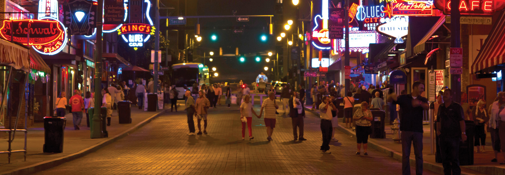 A bustling street in Memphis, Tennessee is illuminated at night by the vibrant neon signs of blues clubs and cafes.