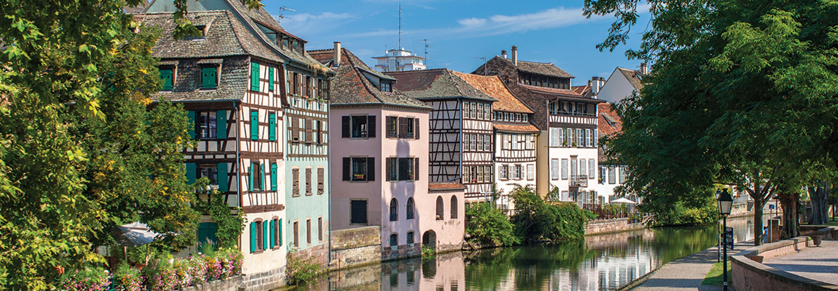 Colorful half-timbered buildings and lush trees line a scenic canal in the Alsace-Lorraine region of France.