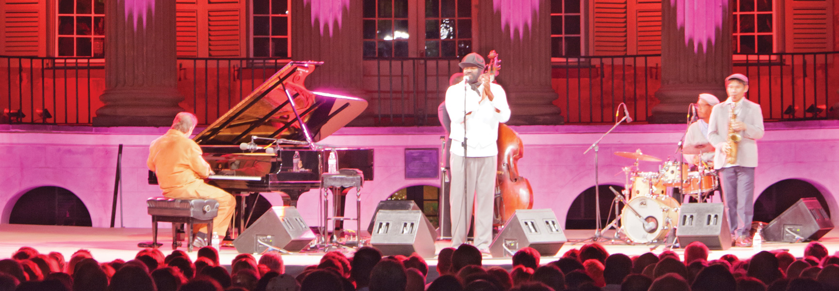 A jazz band performs on an outdoor stage under pink lights for an audience at the Spoleto Festival USA in South Carolina.