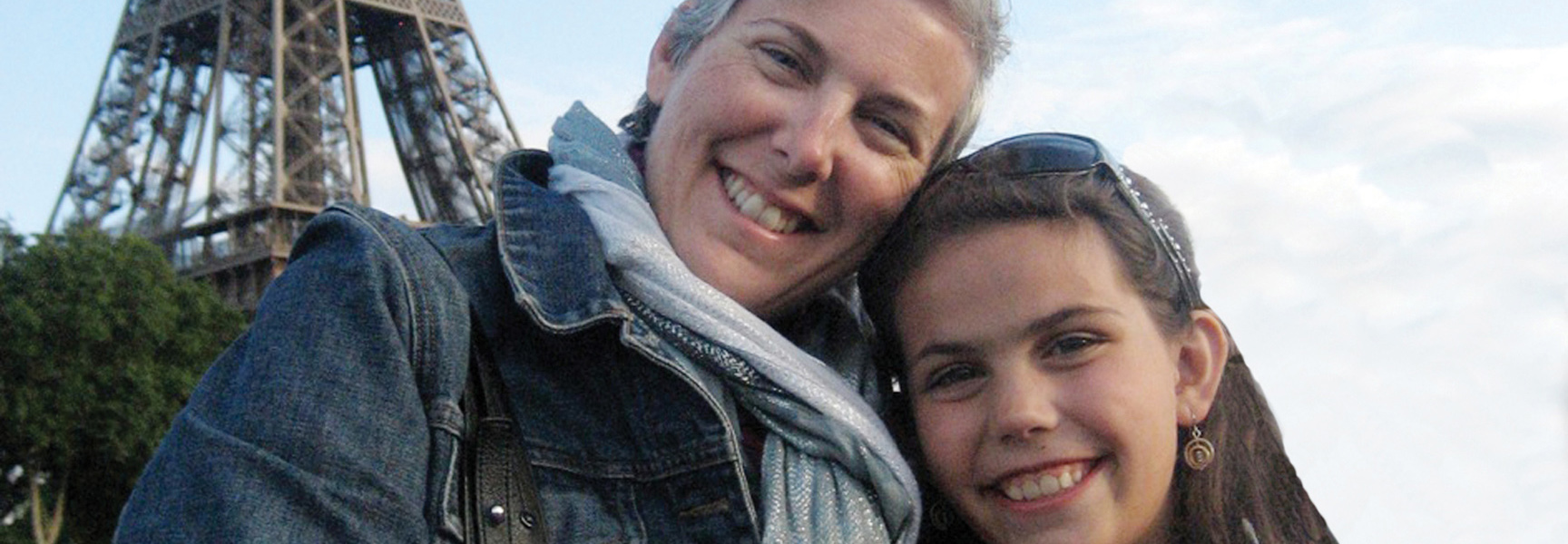 A smiling grandmother and her granddaughter pose together in front of the Eiffel Tower in Paris, France.