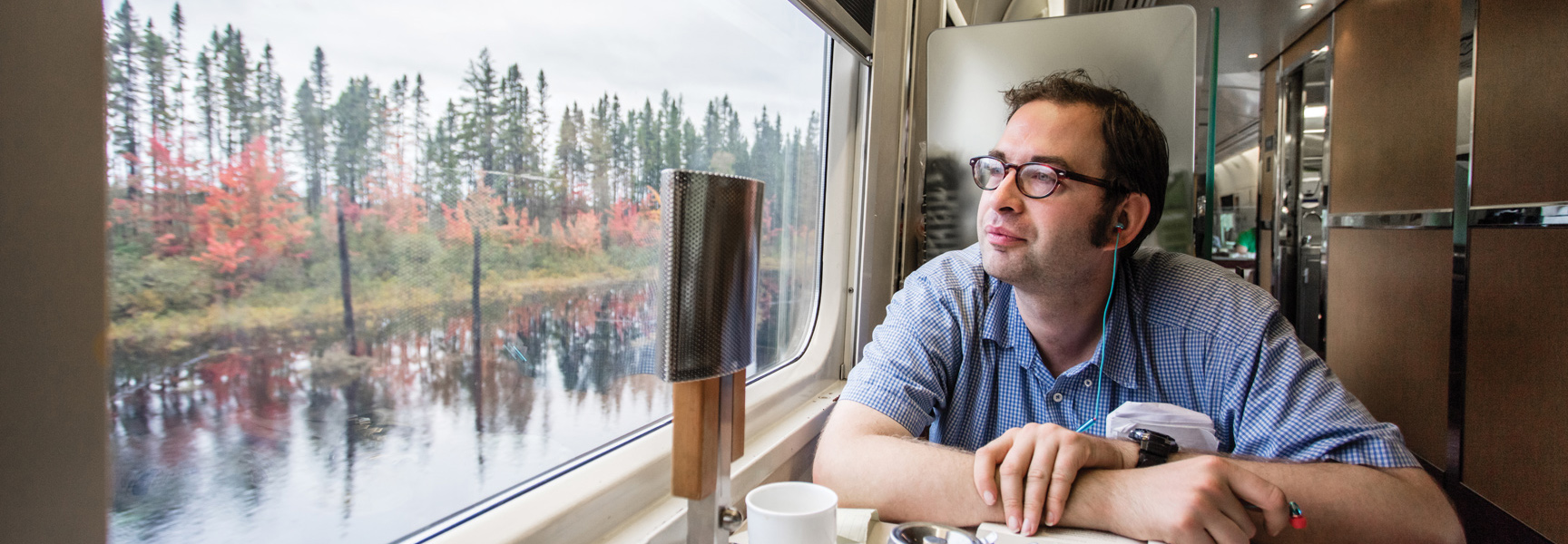 A man on a train looks out the window at the autumn scenery of Québec and the Canadian Maritimes.