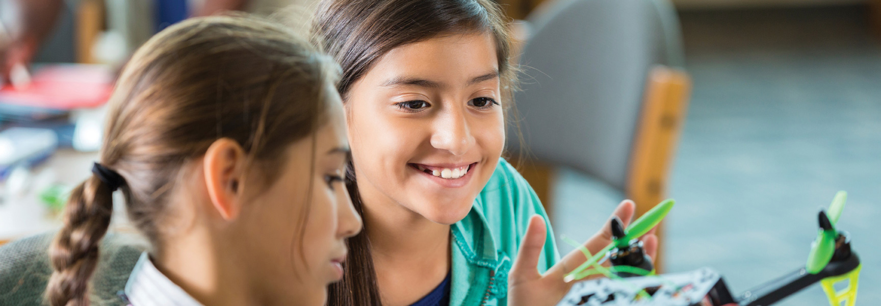 Two young girls in Missouri smile while working together on a hands-on science project involving a small drone.