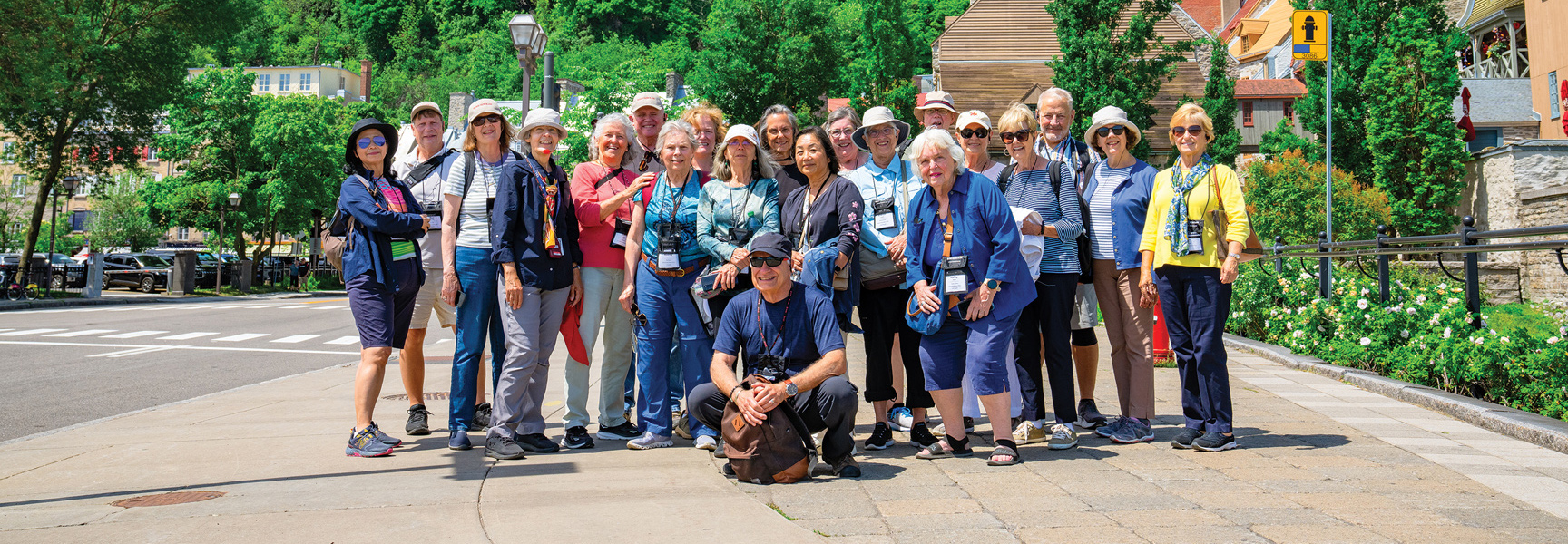 A group of older travelers smiles for a group photo on a sunny, tree-lined street in Québec.