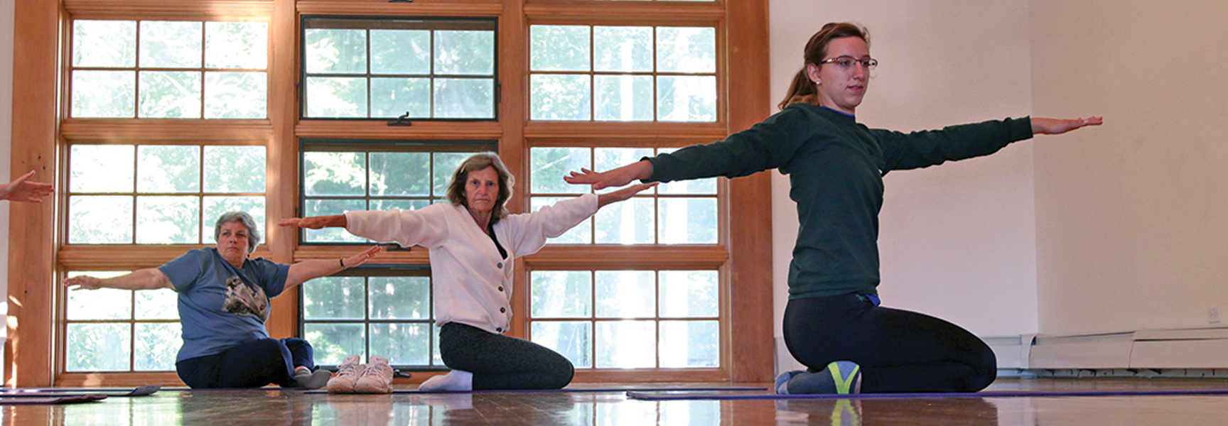 Three women practice a yoga pose with arms outstretched in a studio in North Carolina.