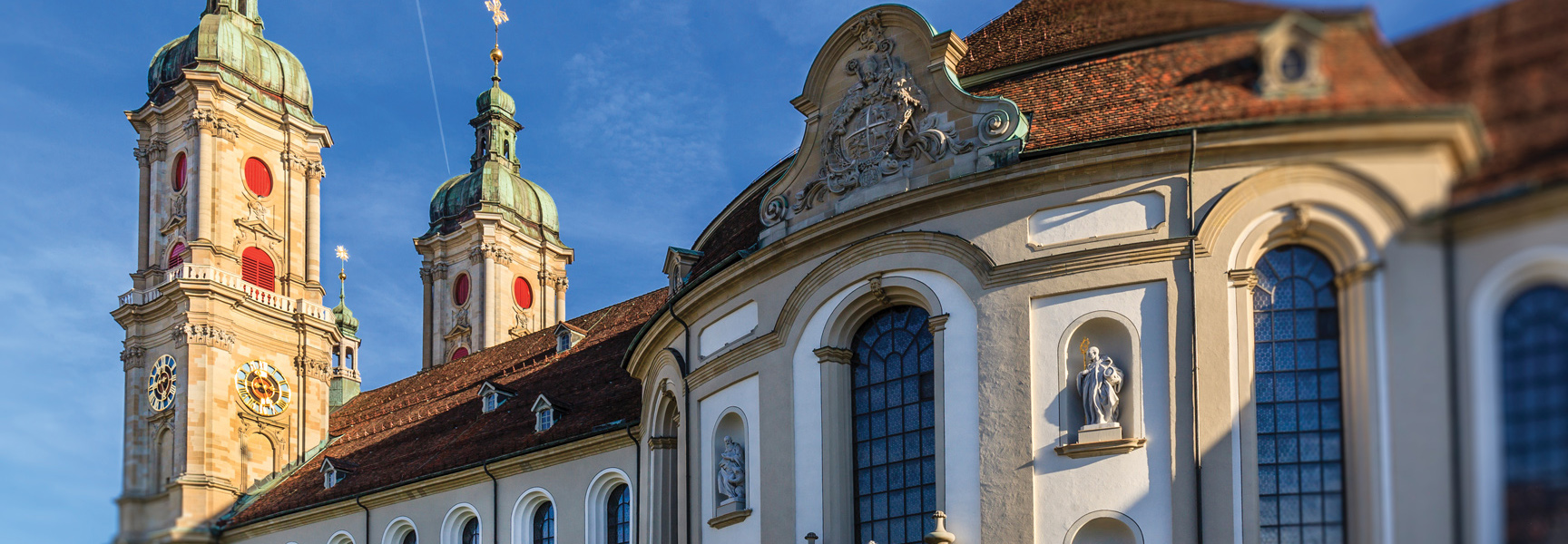 An ornate baroque-style cathedral with twin bell towers against a bright blue sky in Switzerland.
