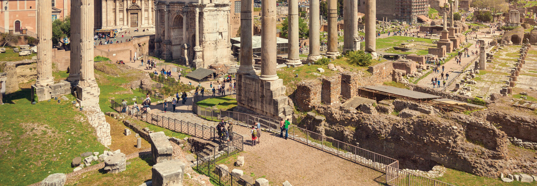Ancient ruins of the Roman Forum in Rome, Italy, featuring stone columns and historical architecture under a bright, cloud-filled blue sky.