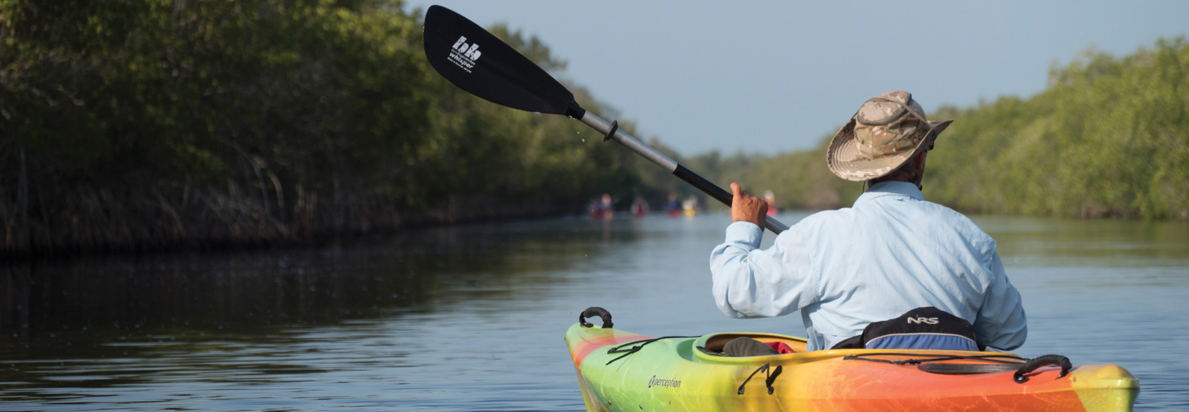 A person in a colorful kayak paddles down a waterway through mangroves in Florida.