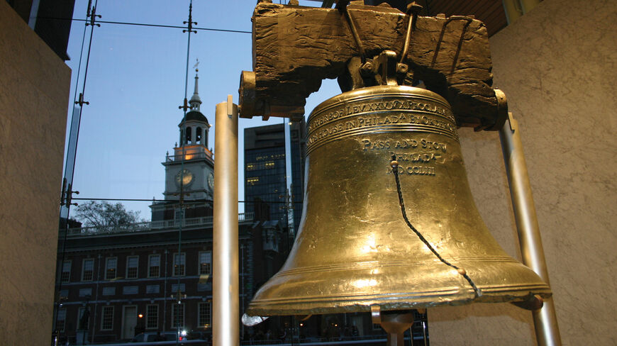 The Liberty Bell in Philadelphia, Pennsylvania, with Independence Hall visible through a large glass window in the background.