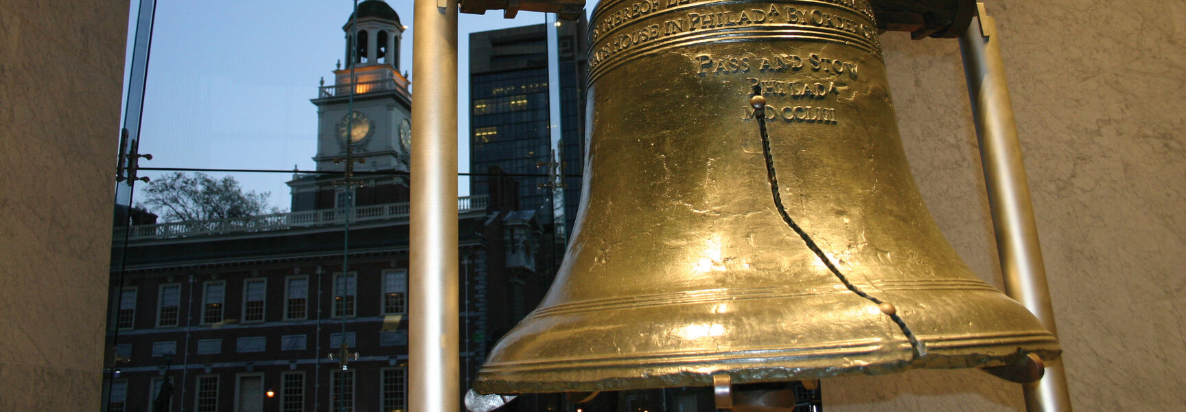 The Liberty Bell in Philadelphia, Pennsylvania, with Independence Hall visible through a large glass window in the background.