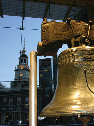 The Liberty Bell in Philadelphia, Pennsylvania, with Independence Hall visible through a large glass window in the background.
