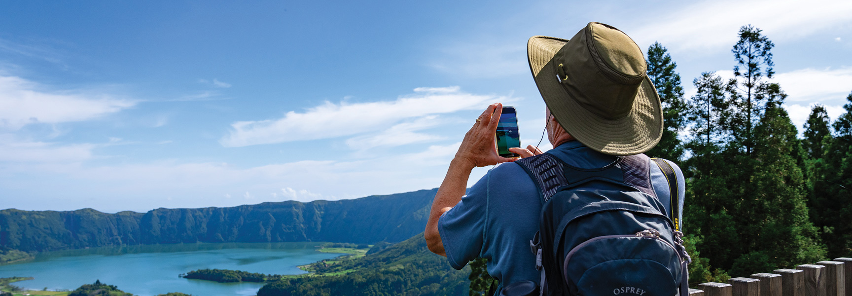 A person in a hat takes a photo of a volcanic crater lake in the Azores.