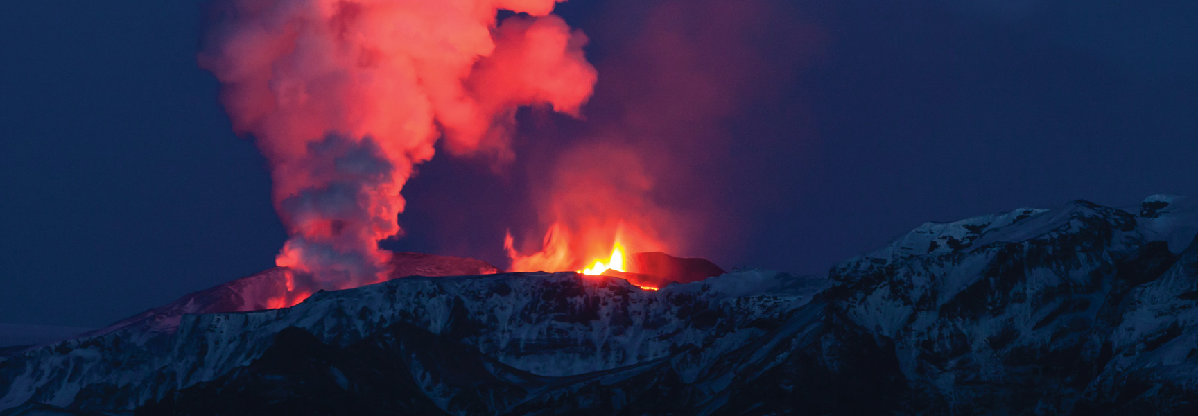 An Icelandic volcano erupts at night, sending glowing red smoke and lava over snow-covered mountains.