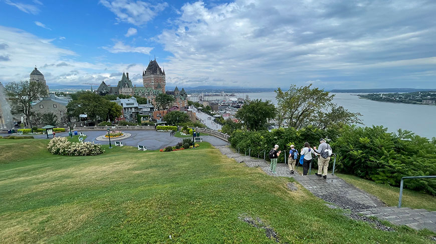 A group hikes down stone stairs overlooking historic Old Quebec City and the iconic Fairmont Le Château Frontenac along the St. Lawrence River.