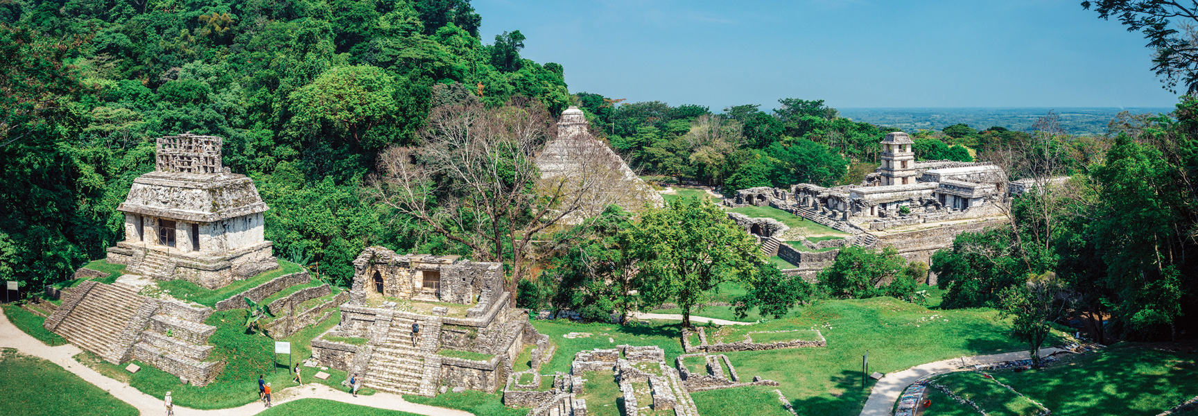 An aerial view shows the ancient stone ruins and temples of an archaeological site surrounded by the lush, green jungle in Chiapas, Mexico.