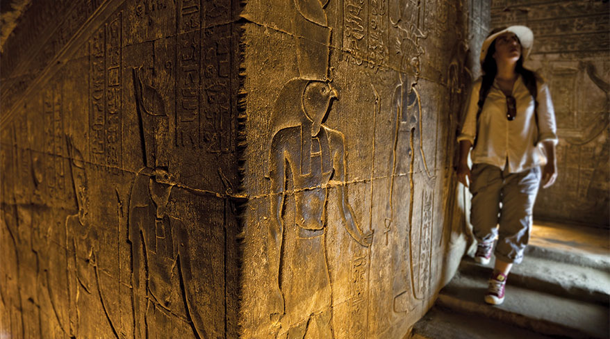 A woman explores the ancient hieroglyphics carved into the stone walls of a temple in Luxor, Africa.
