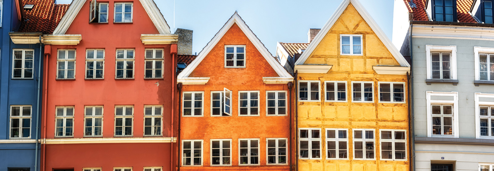 A row of brightly colored historic buildings with gabled roofs and many windows stand side-by-side in Copenhagen, Denmark.