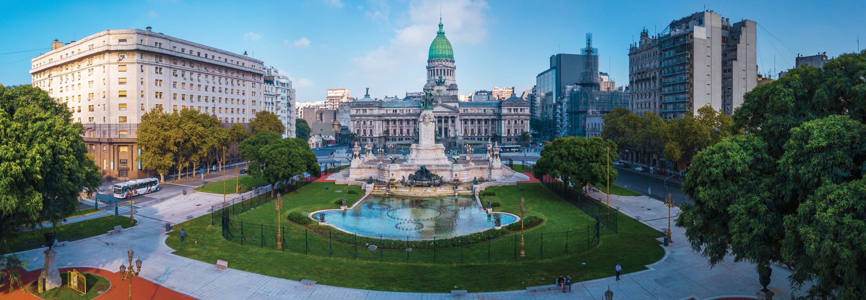 A panoramic view of the Palace of the Argentine National Congress across a plaza with a large fountain and gardens in Buenos Aires, Argentina.