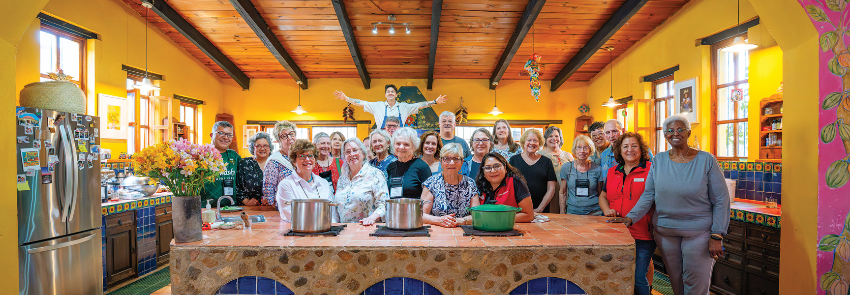 A large group of people smiles for a photo in a colorful kitchen during a cooking class in Mexico.
