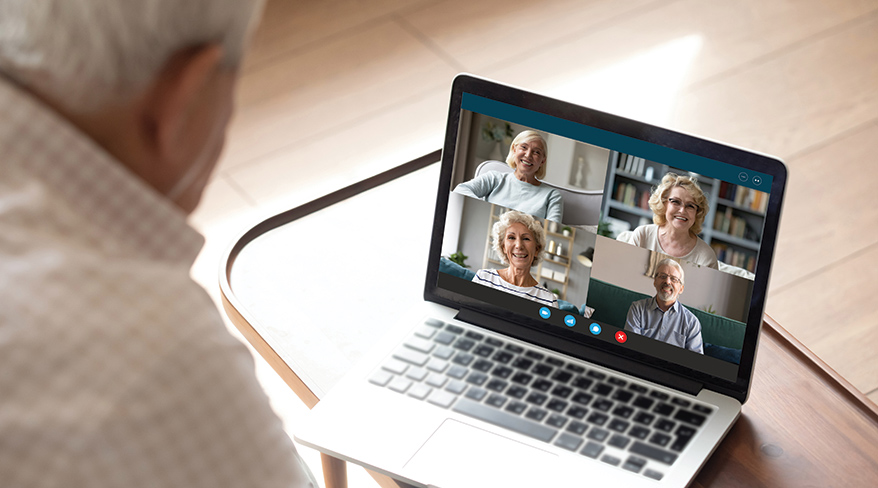An older man participates in an online lecture, viewing several other seniors on his laptop screen during a video call.