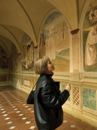 A woman looks up at historical religious frescoes on a hallway wall while living and learning in Siena, Italy.