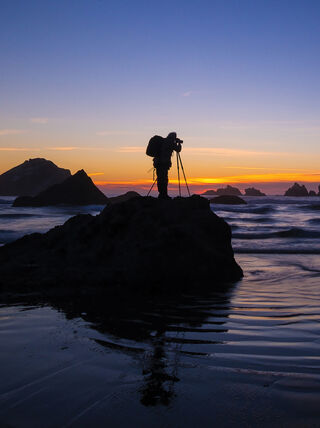 Silhouette of a photographer capturing a sunset landscape on a rocky beach, illustrating advanced digital photography techniques.