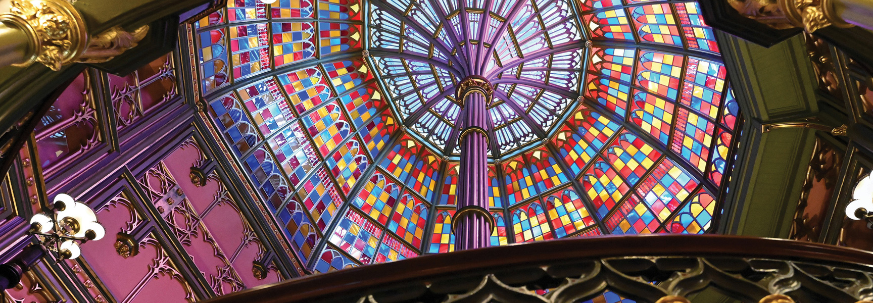 A view looking up at a vibrant, multi-colored stained-glass ceiling in a historic building in Louisiana.