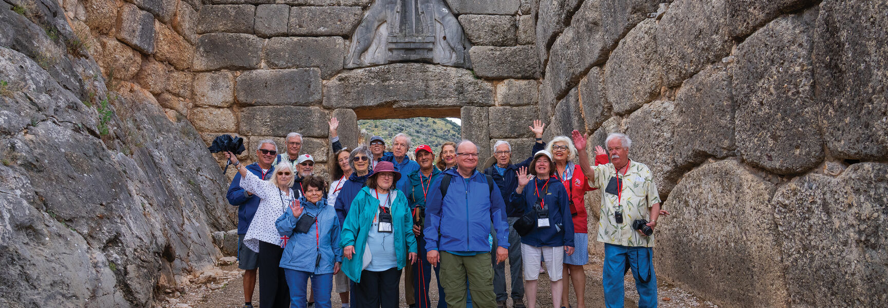 A group of travelers smiles in front of the ancient Lion Gate in Greece during a mythical journey learning adventure about ancient stories.