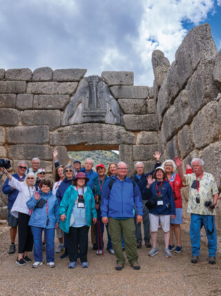 A group of travelers smiles in front of the ancient Lion Gate in Greece during a mythical journey learning adventure about ancient stories.