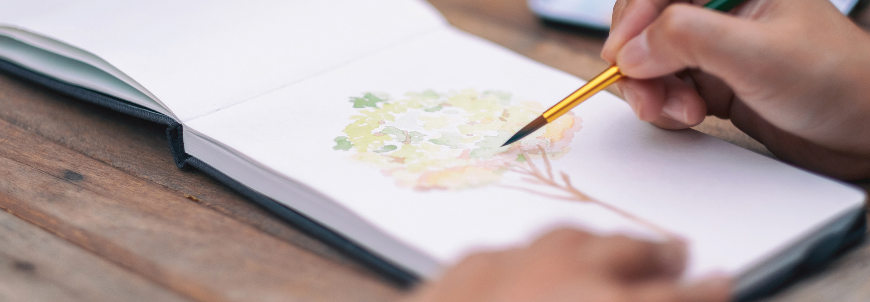 A person uses a small brush to paint a tree with watercolors in a sketchbook during a workshop in the Laurel Highlands, Pennsylvania.