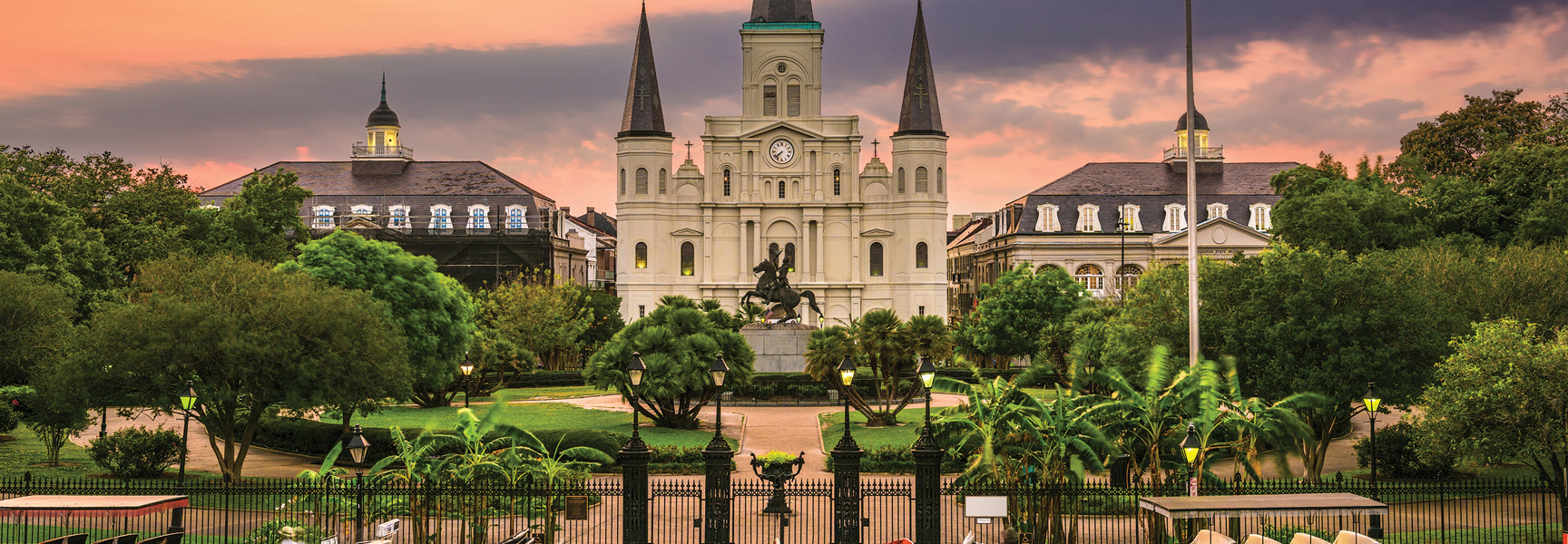 St. Louis Cathedral in Jackson Square, New Orleans, Louisiana, is pictured at sunset, surrounded by lush trees and gardens.