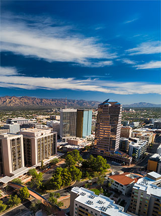 An aerial view of downtown Tucson, Arizona buildings under a blue sky with the Santa Catalina Mountains in the background.