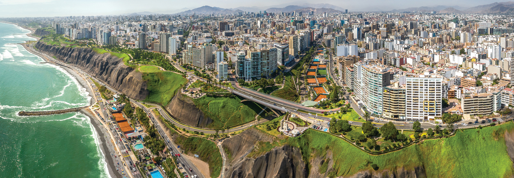 An aerial panoramic view of the city of Lima, Peru, where the bustling city meets the Pacific Ocean along dramatic cliffs.