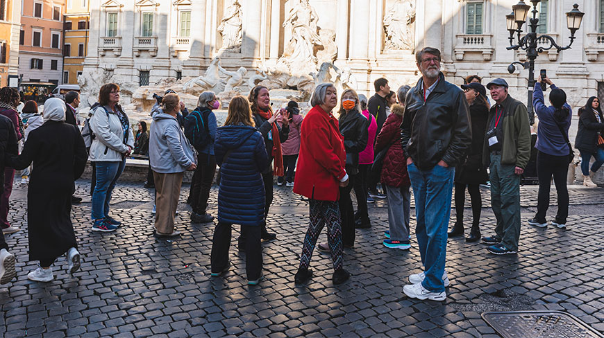 A crowd of tourists gathers on a cobblestone square in front of the Trevi Fountain in Rome.