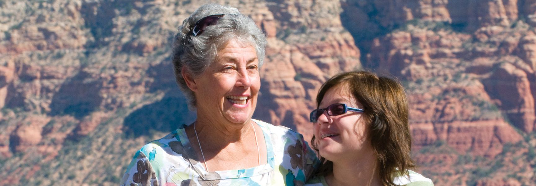 A grandmother and her grandchild smile together in front of the stunning red rock canyons of Arizona.