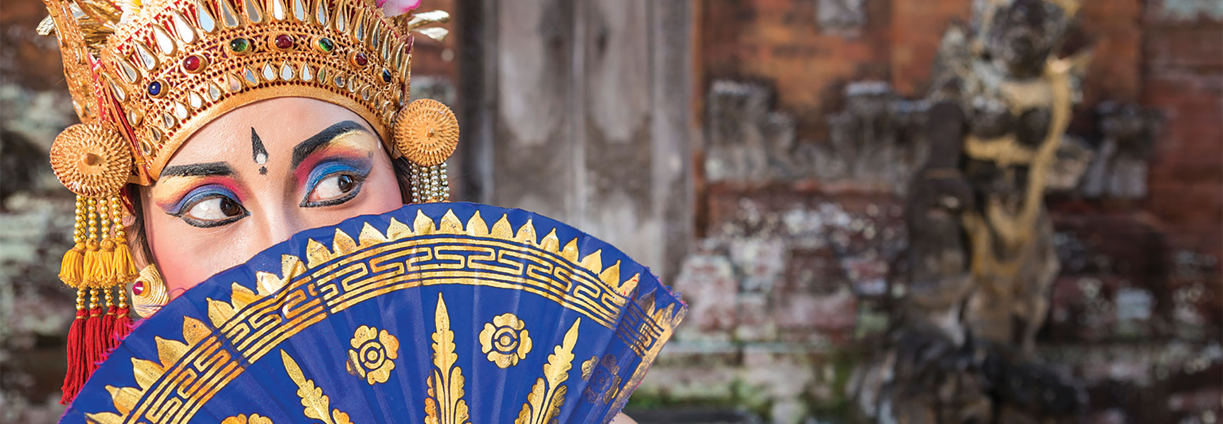 A dancer in ornate traditional headwear and makeup holds a blue and gold fan, illustrating sacred rituals of movement in the ancient world.