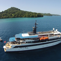 The Variety Voyager sails through the turquoise waters off the coast of a tree-covered island in Greece or Turkey.