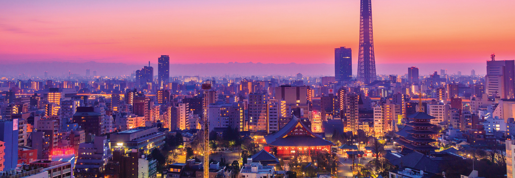 The Tokyo, Japan skyline, including the Skytree and Senso-ji temple, glows with city lights under a vibrant pink and orange sunset.