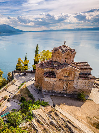 A high-angle view of the historic St. John Church on a cliff overlooking the expansive Lake Ohrid in North Macedonia.