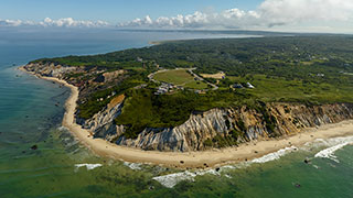 An aerial view of the dramatic, sandy cliffs and lush green landscape of Martha's Vineyard in Massachusetts, meeting the ocean.