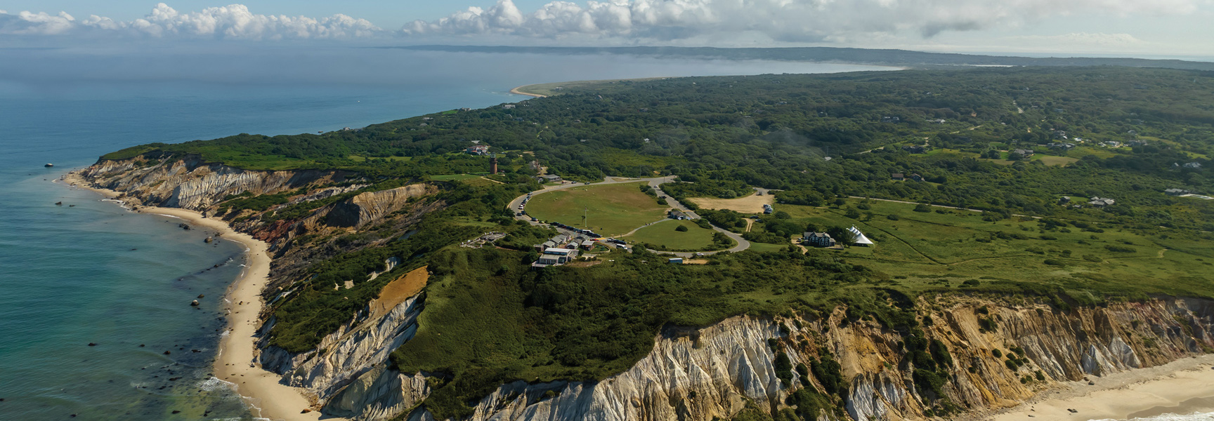 An aerial view of the stunning coastal cliffs and lush green landscape of Martha's Vineyard, Massachusetts, meeting the calm blue sea.