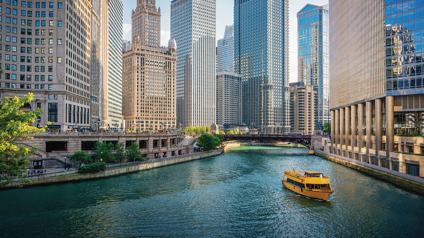 A yellow tour boat navigates the Chicago River, passing iconic skyscrapers under a clear blue sky during a Great Lakes Floating Campus voyage.