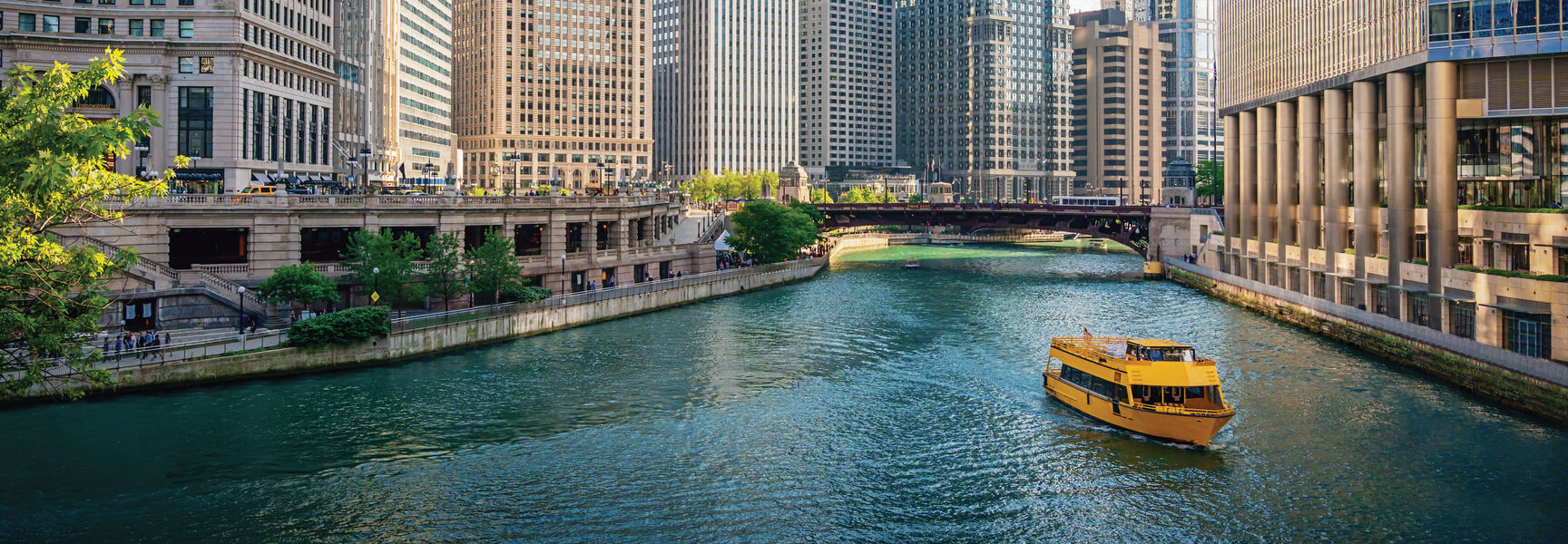 A yellow tour boat navigates the Chicago River, passing iconic skyscrapers under a clear blue sky during a Great Lakes Floating Campus voyage.