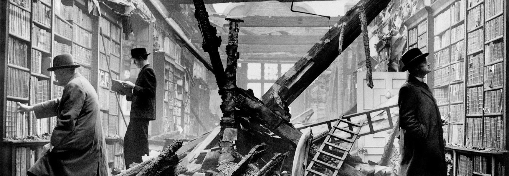 A black and white photo shows men calmly selecting books from shelves in a library destroyed during World War II.